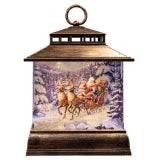 A decorative lantern-shaped Christmas ornament with a dark brown wood-grain frame and a circular top handle. Inside the clear front panel is a festive winter scene showing Santa Claus in a sleigh pulled by three reindeer, set against a snowy forest at night.