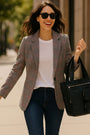 Woman in a plaid blazer and sunglasses holding a black handbag on a city street.