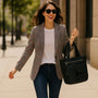 Woman in a plaid blazer and sunglasses holding a black handbag on a city street.