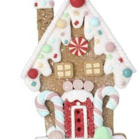 A gingerbread house Christmas ornament with white icing details, candy decorations, a red door, and a red hanging ribbon on a white background.