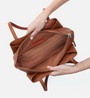 Brown leather bag held by a person on a white background
