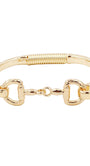 A gold-tone metal bracelet featuring a textured band, a coiled spring detail on one side, and two horsebit-style D-rings connected by a small central link, shown on a plain white background.