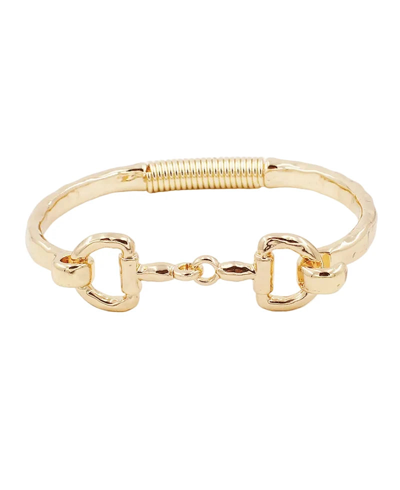 A gold-tone metal bracelet featuring a textured band, a coiled spring detail on one side, and two horsebit-style D-rings connected by a small central link, shown on a plain white background.