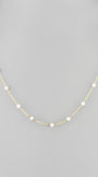 A delicate gold chain necklace featuring evenly spaced, small white pearl beads, displayed on a neutral gray background.