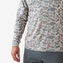 A close-up of a person wearing a long-sleeve performance shirt with an abstract organic camouflage pattern in gray, taupe, and off-white, paired with gray athletic pants.