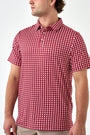 A man wearing a short-sleeve polo shirt with a red and white geometric checkered pattern, shown from the side against a plain white studio background.