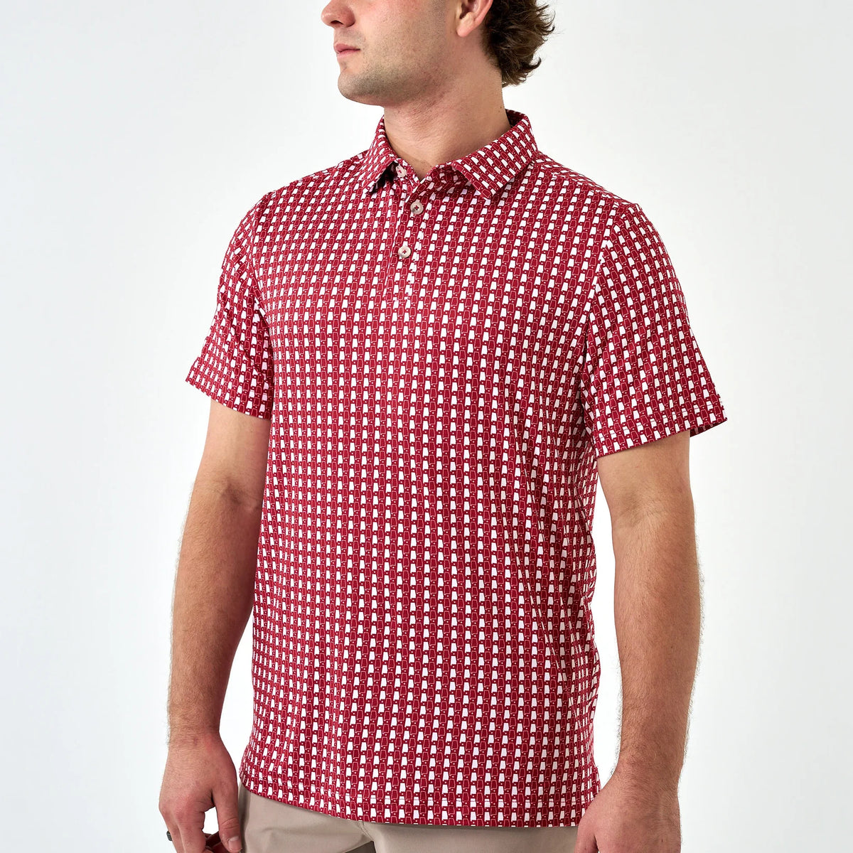 A man wearing a short-sleeve polo shirt with a red and white geometric checkered pattern, shown from the side against a plain white studio background.