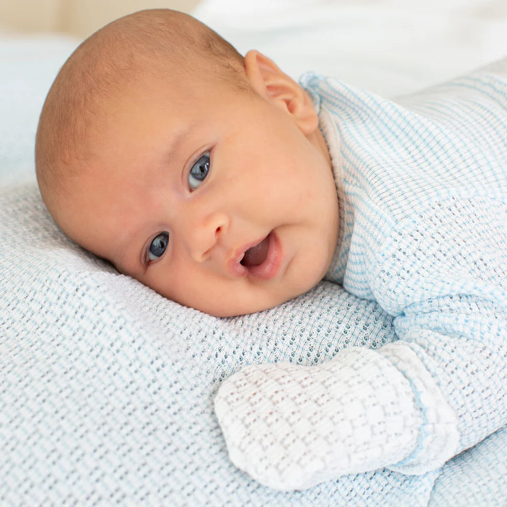 Newborn baby lying on a textured blanket wearing a light blue outfit.