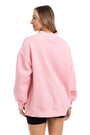 A woman shown from the back wearing an oversized light pink crewneck sweatshirt and black shorts against a plain white background.