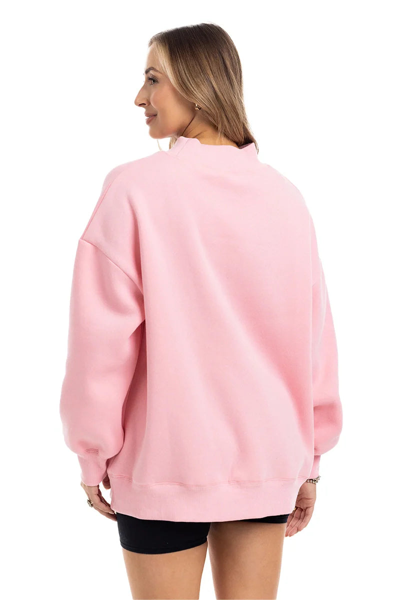 A woman shown from the back wearing an oversized light pink crewneck sweatshirt and black shorts against a plain white background.