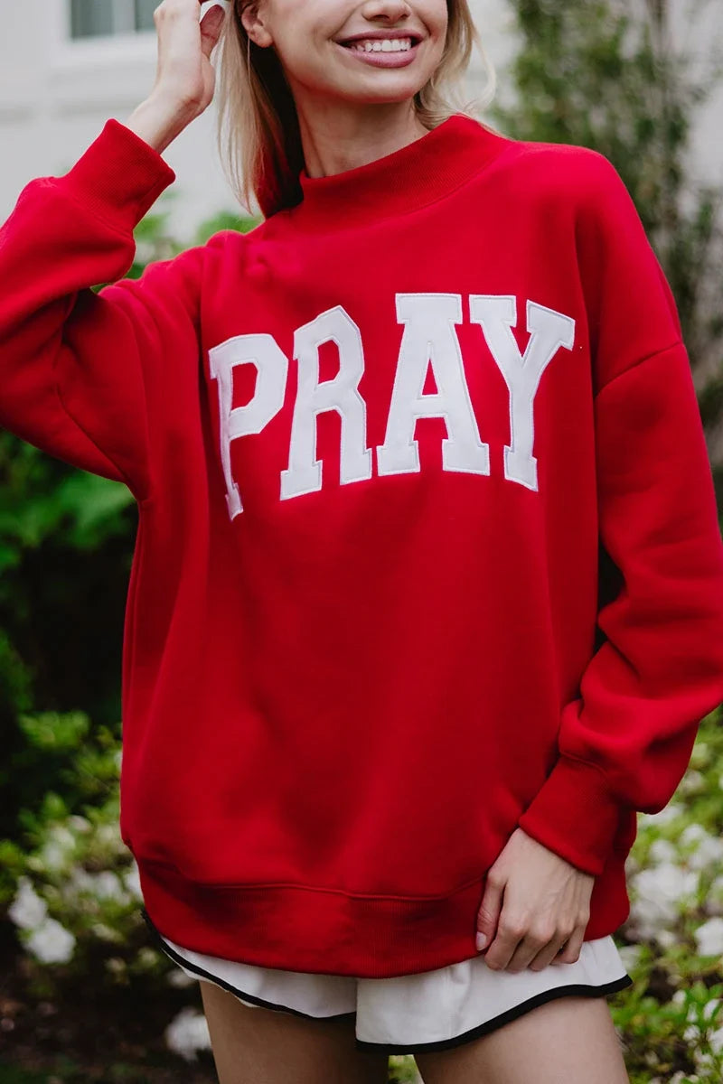 Person wearing a red sweatshirt with 'PRAY' printed on it, standing outdoors.