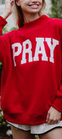 Person wearing a red sweatshirt with 'PRAY' printed on it, standing outdoors.