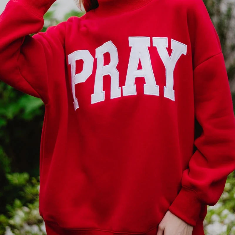 Person wearing a red sweatshirt with 'PRAY' printed on it, standing outdoors.