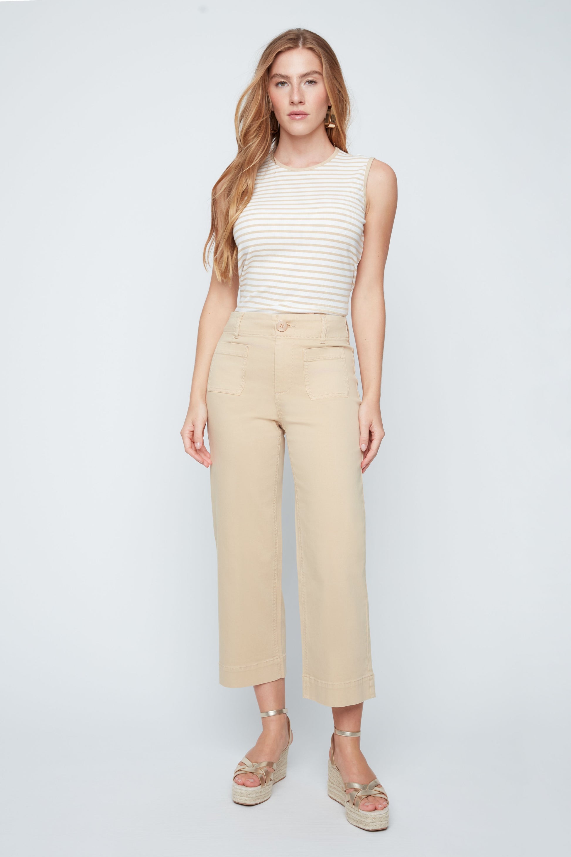 Woman wearing a white sleeveless top and beige pants on a white background