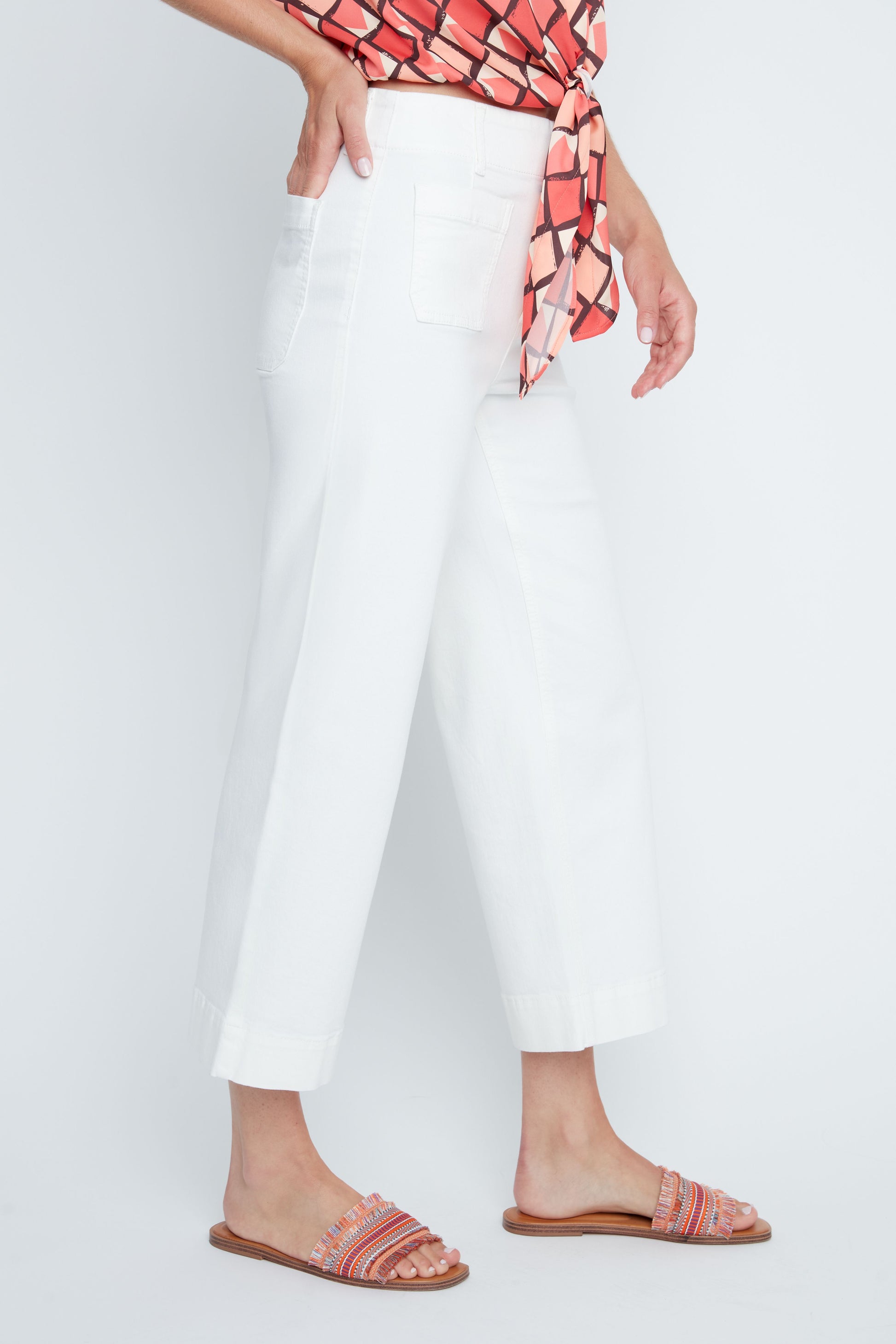 Person wearing white pants with a red and pink patterned top and sandals on a white background