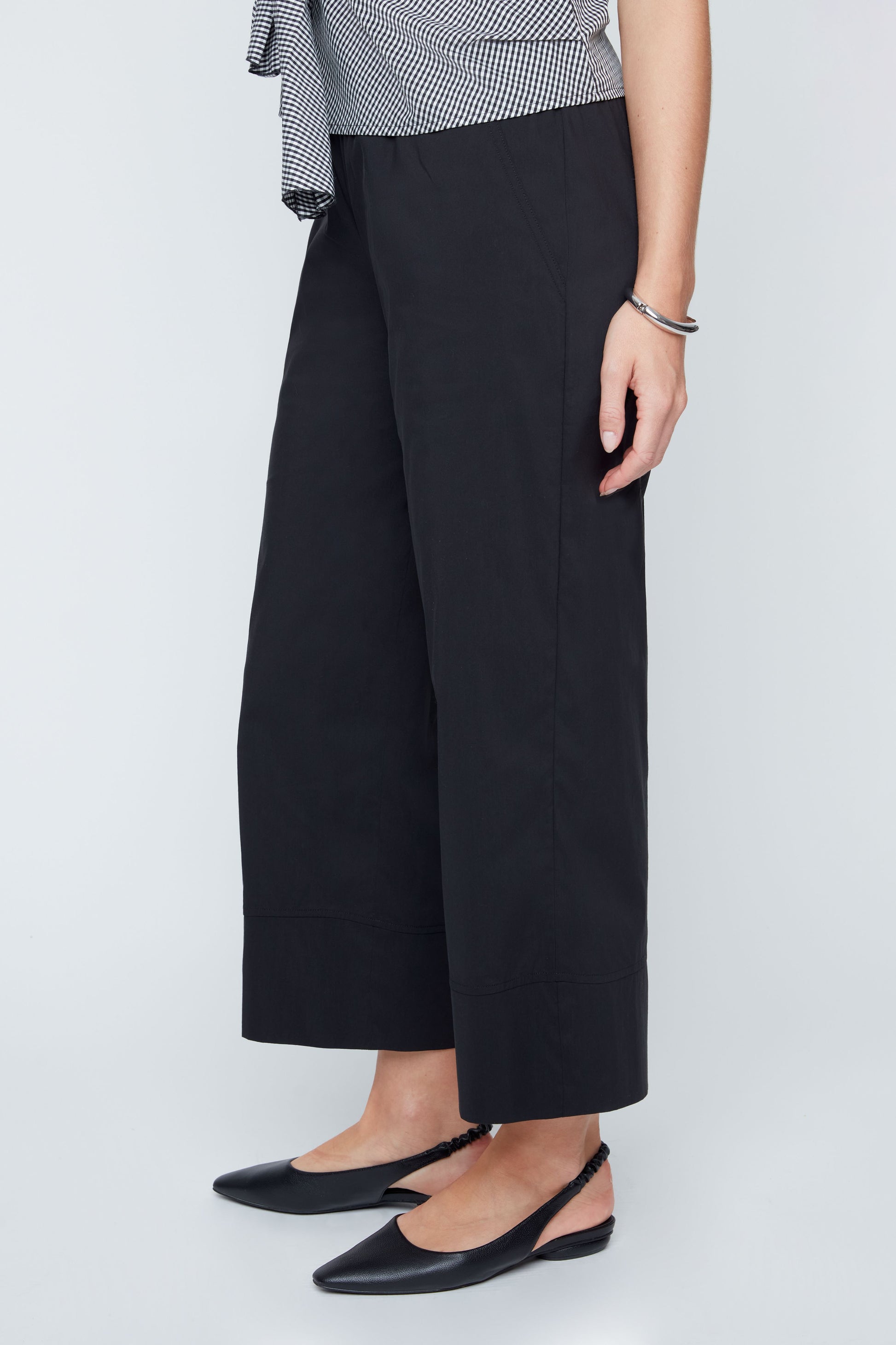 Person wearing black wide-leg pants and a checkered top on a white background