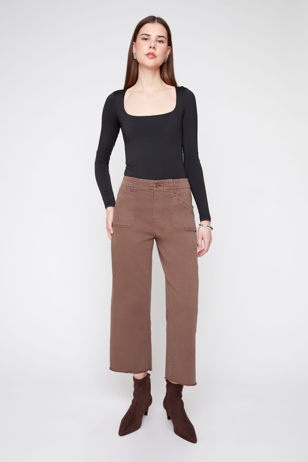 Woman wearing a black long-sleeve top and brown pants on a white background