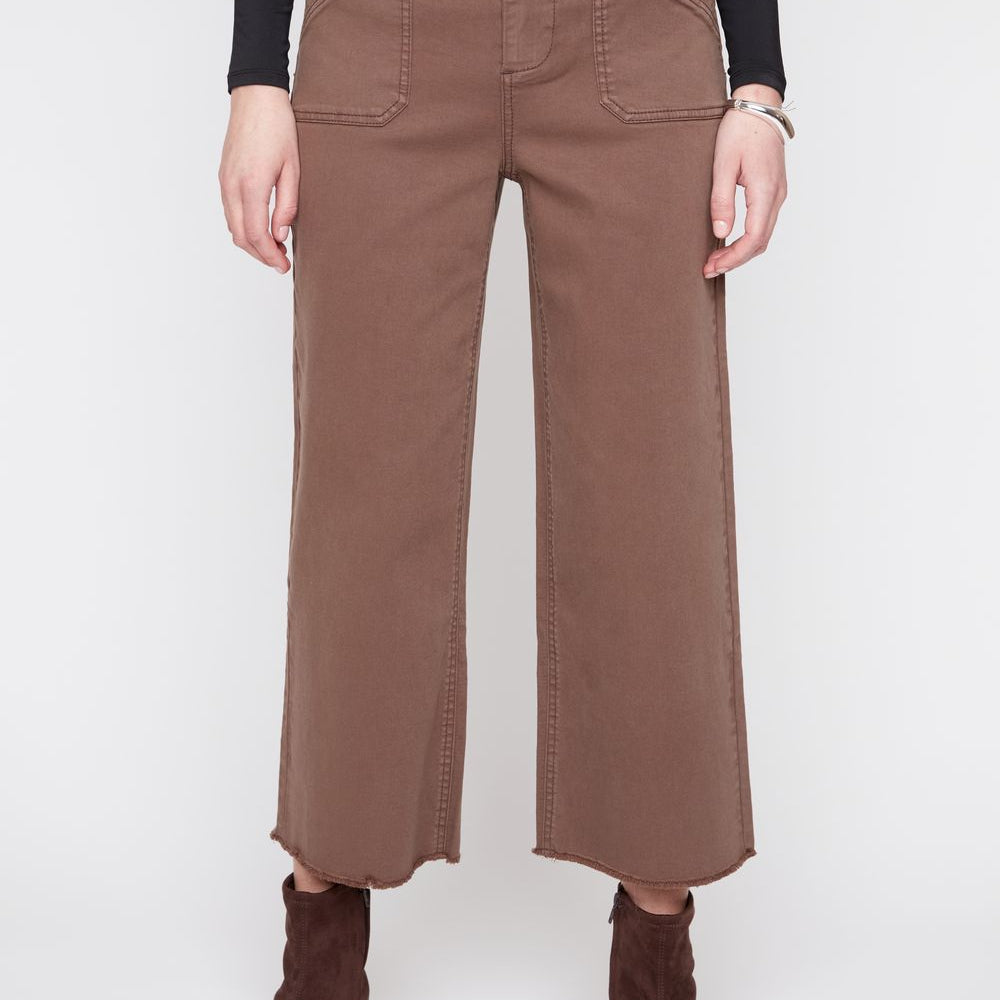 A model wearing brown wide-leg cropped pants with a black long-sleeve top and dark brown pointed-toe ankle boots, shown from the waist down against a light gray studio background.