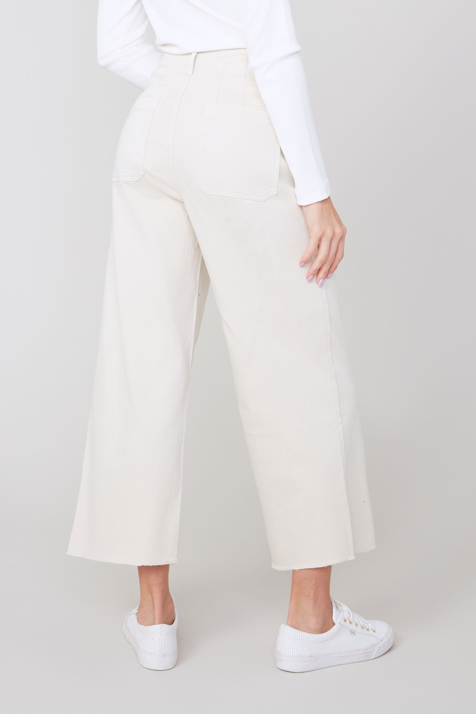 Person wearing light khaki wide-leg pants and a white shirt on a plain background