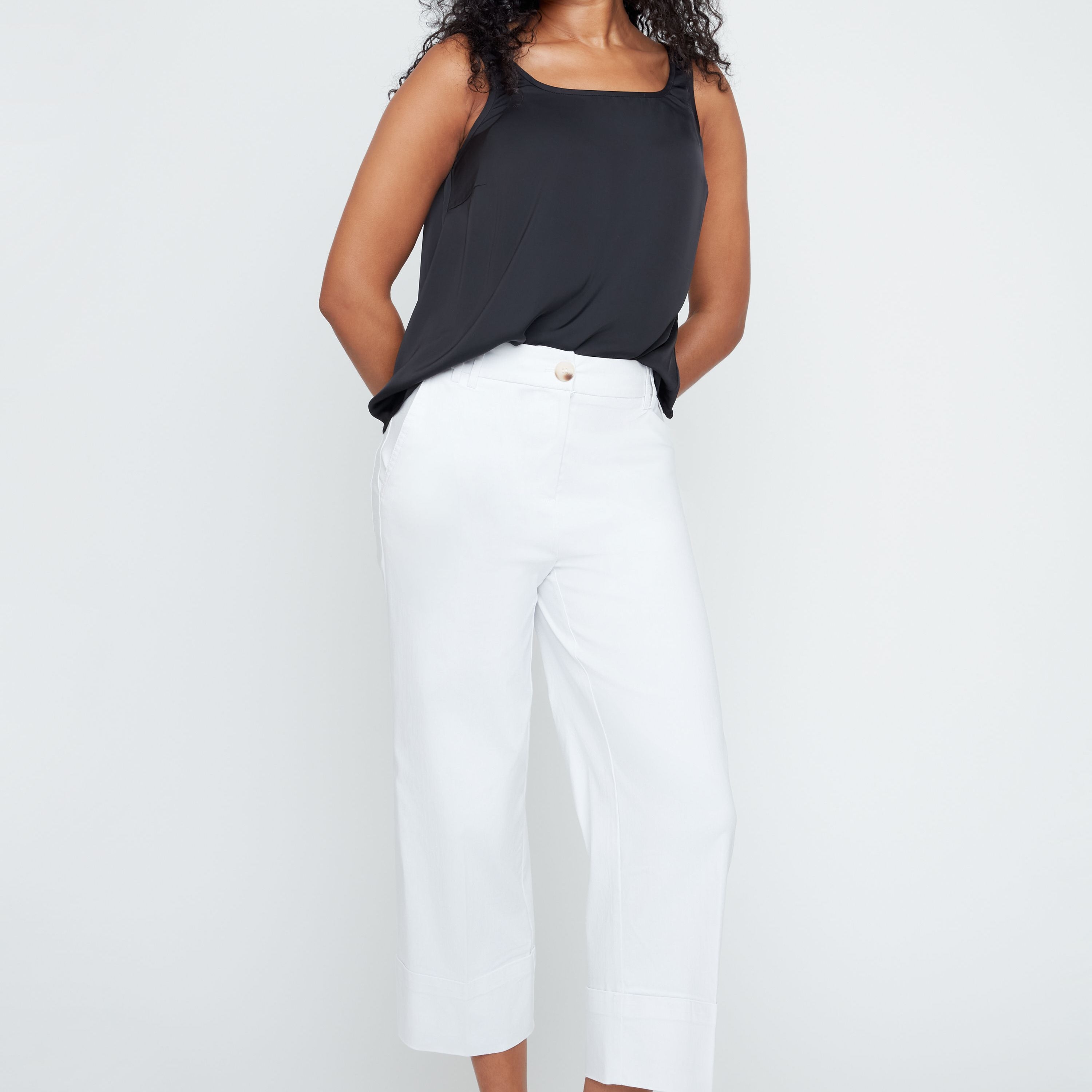 Woman wearing a black sleeveless top and white pants on a white background