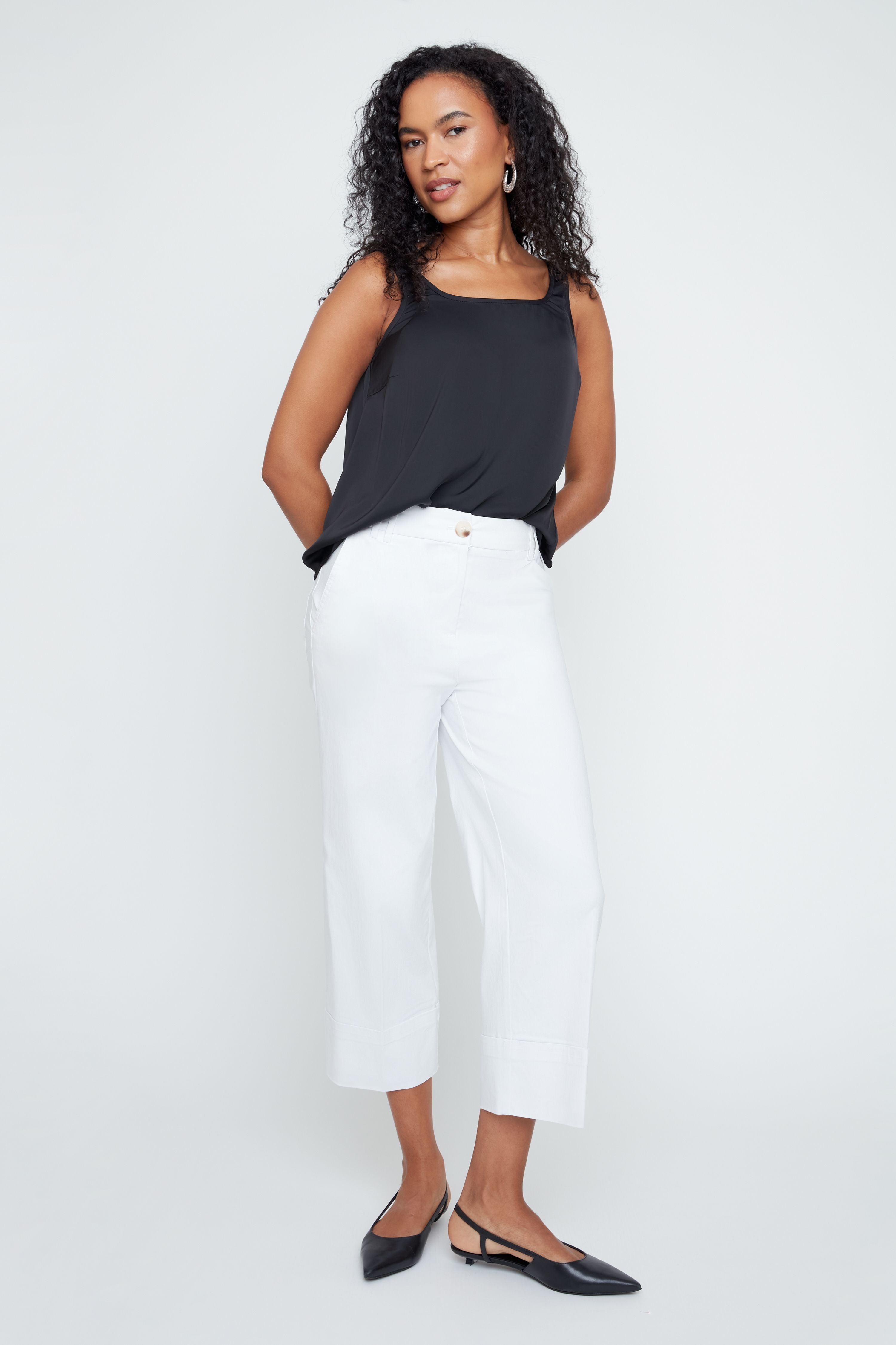 Woman wearing a black sleeveless top and white pants on a white background