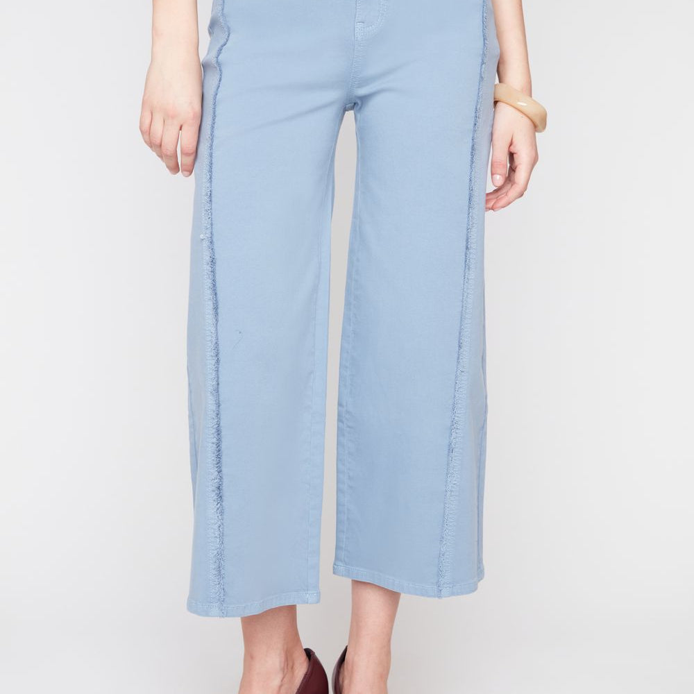 A model wearing light blue cropped wide-leg pants, a light blue satin top, and dark burgundy pointed-toe heels, shown from the waist down against a light gray studio background.