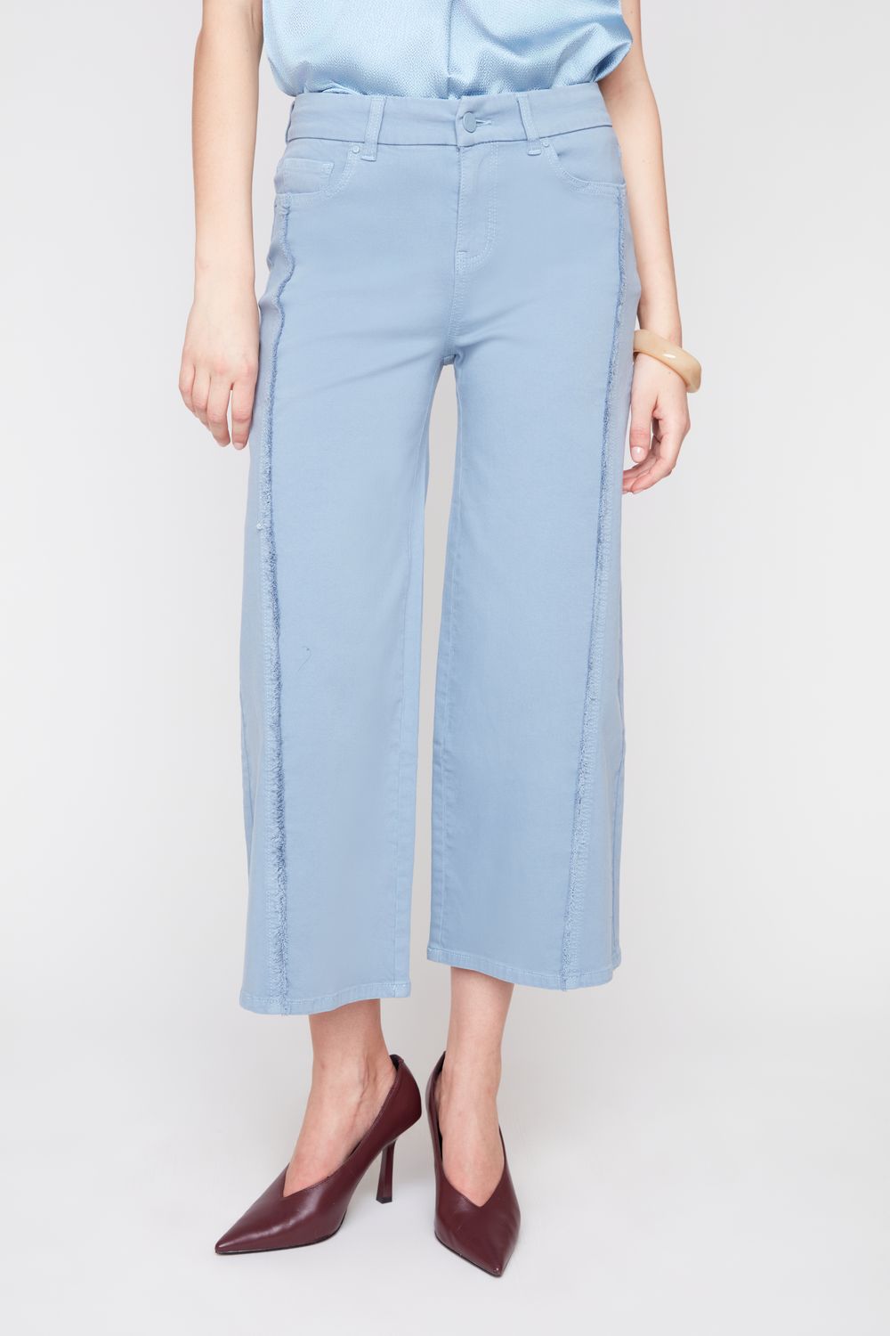 A model wearing light blue cropped wide-leg pants, a light blue satin top, and dark burgundy pointed-toe heels, shown from the waist down against a light gray studio background.