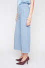 A model wearing light blue wide-leg cropped jeans, a light blue satin top, and dark burgundy pointed-toe heels, shown from the waist down against a plain light gray studio background.