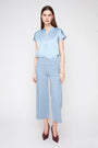 A woman modeling a light blue satin short-sleeve top and matching light blue cropped trousers against a plain light gray studio background.