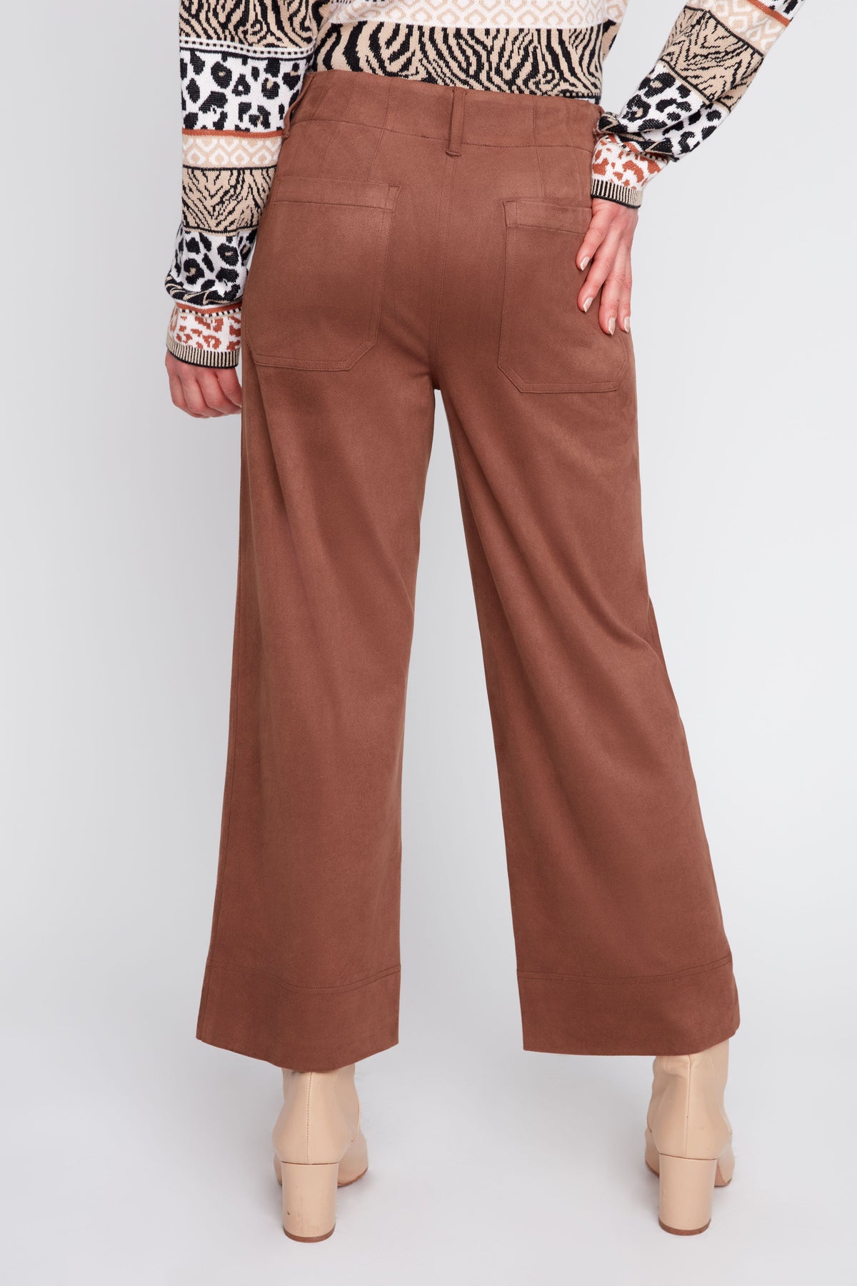 A person shown from the back wearing wide-leg cropped brown pants, a patterned top, and beige heeled boots against a light gray studio background.