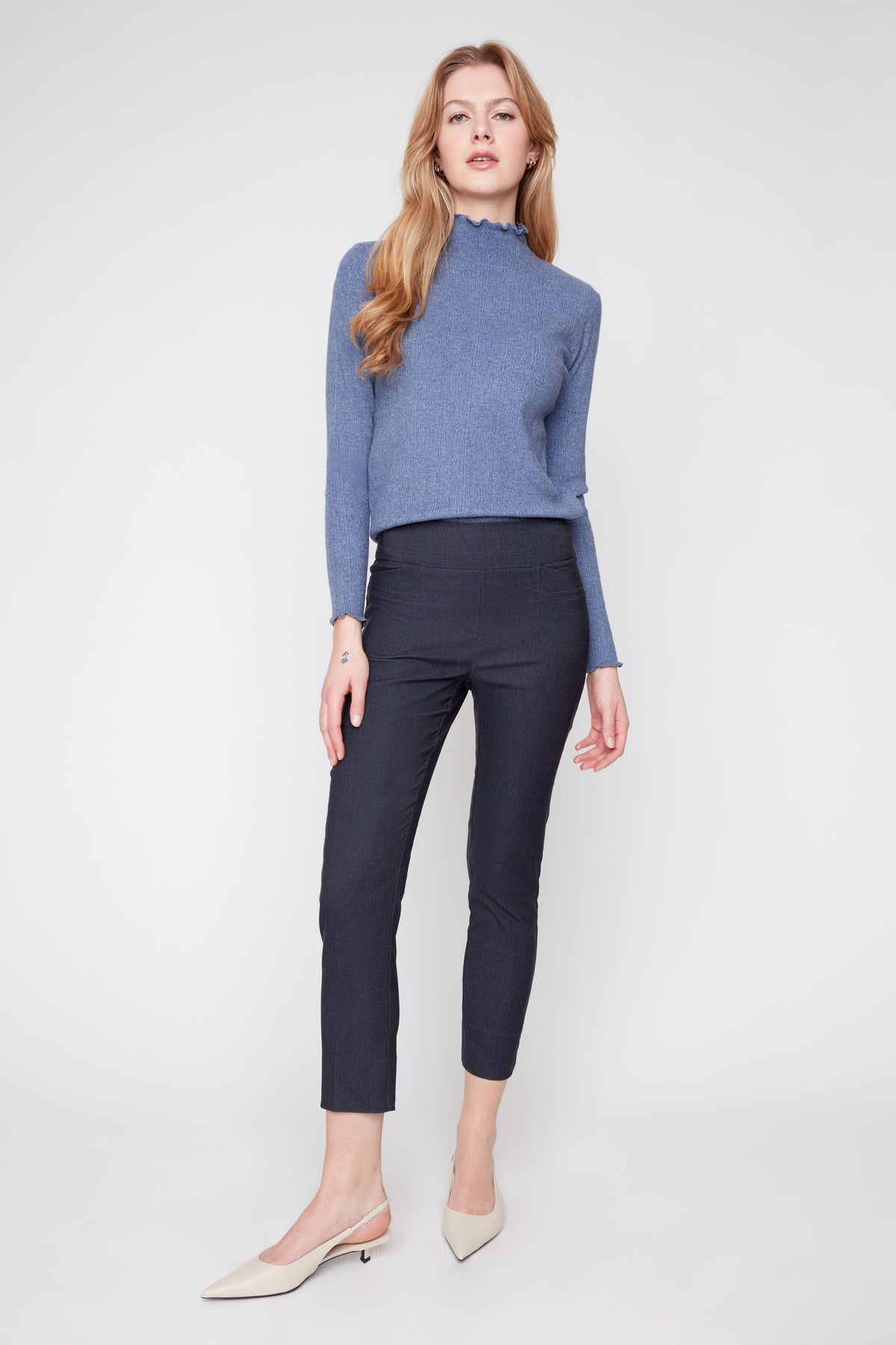 Woman wearing a blue long-sleeve top and black pants on a white background