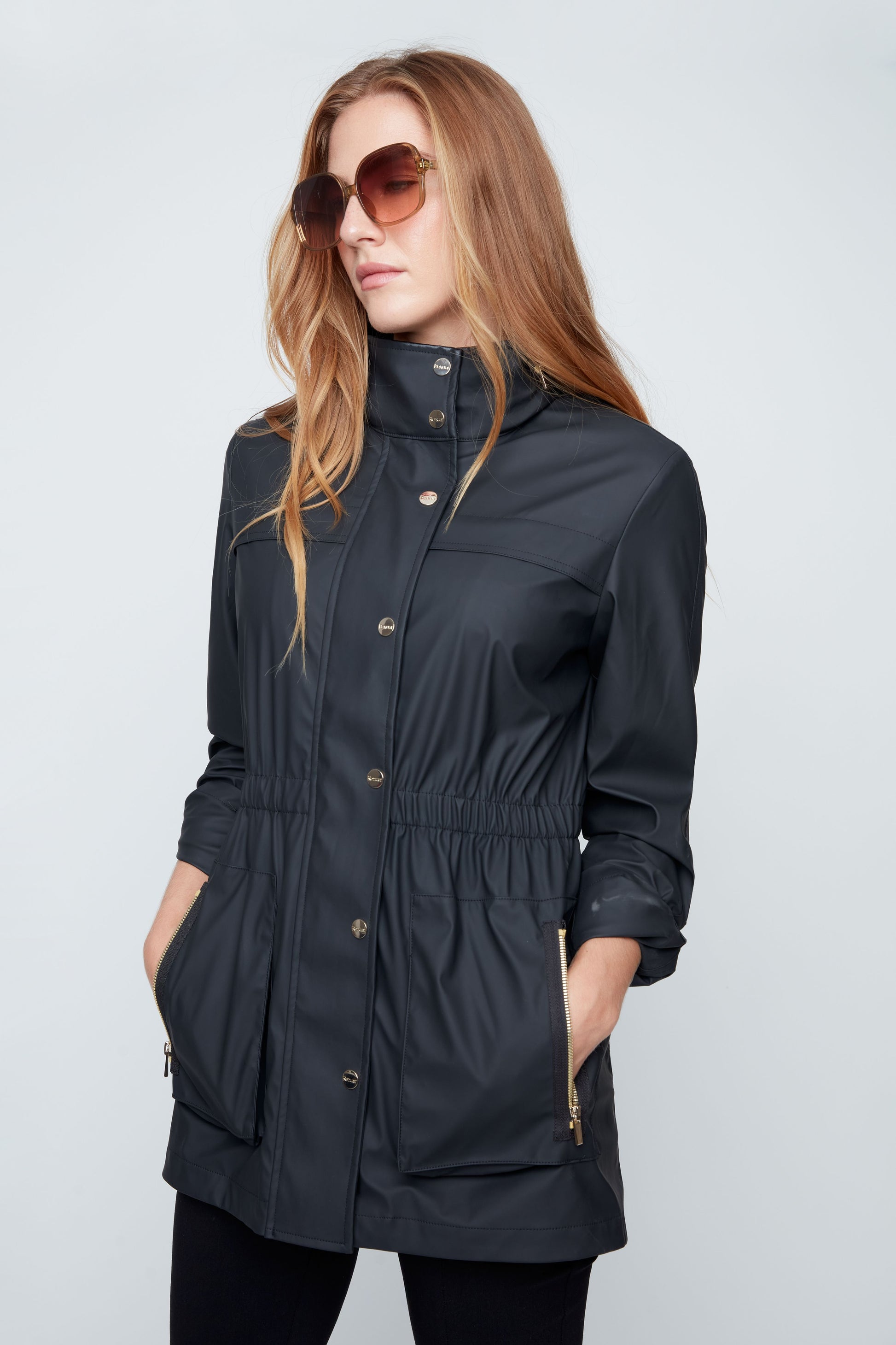 Woman wearing a black raincoat with sunglasses on a light gray background