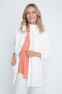Woman wearing a white jacket over a coral top and white pants on a light gray background