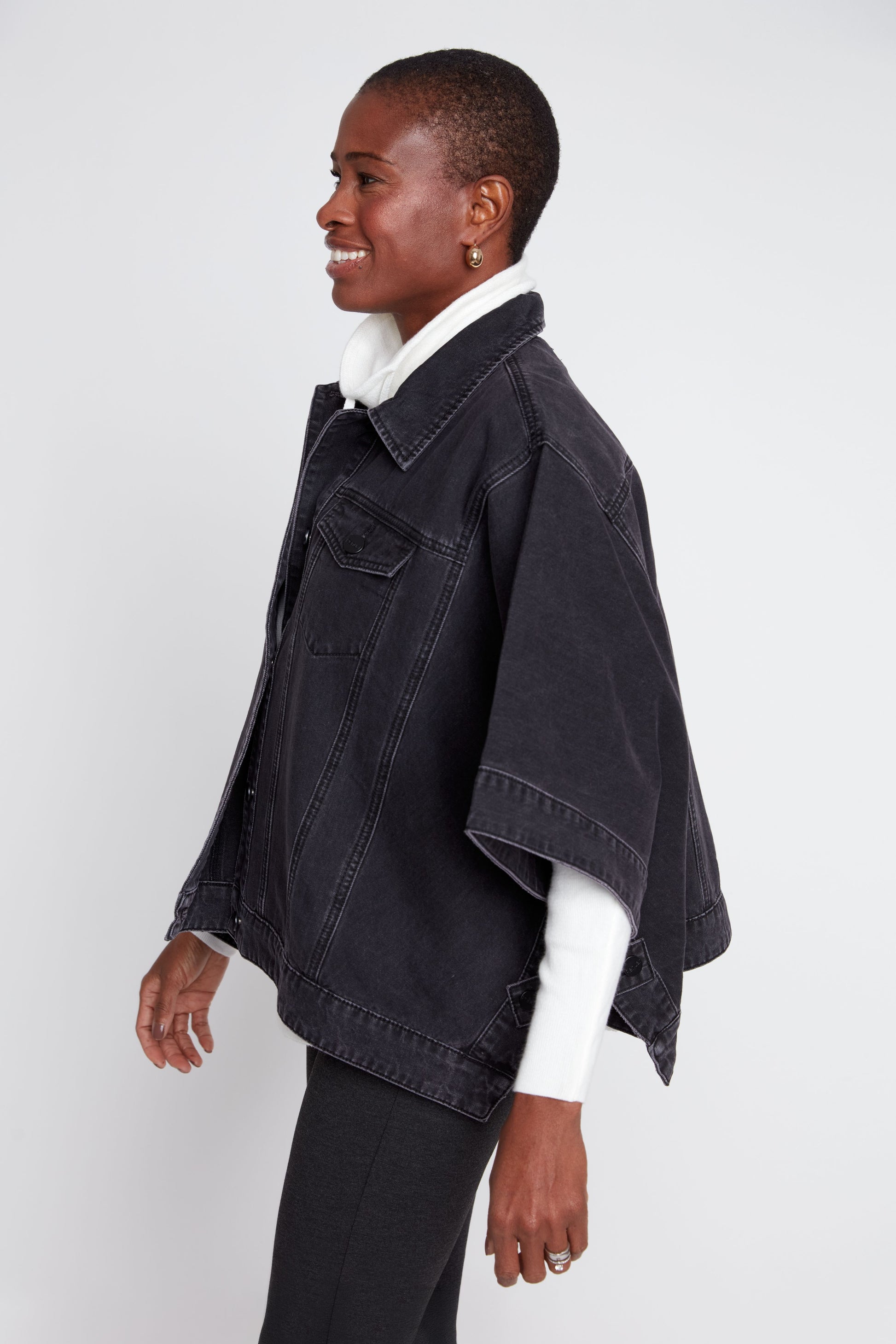 Person wearing a black denim jacket with white lining on a white background