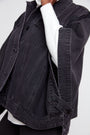 A close-up of a person wearing a dark washed denim jacket over a white long-sleeve top, showing the texture and details of the jacket.