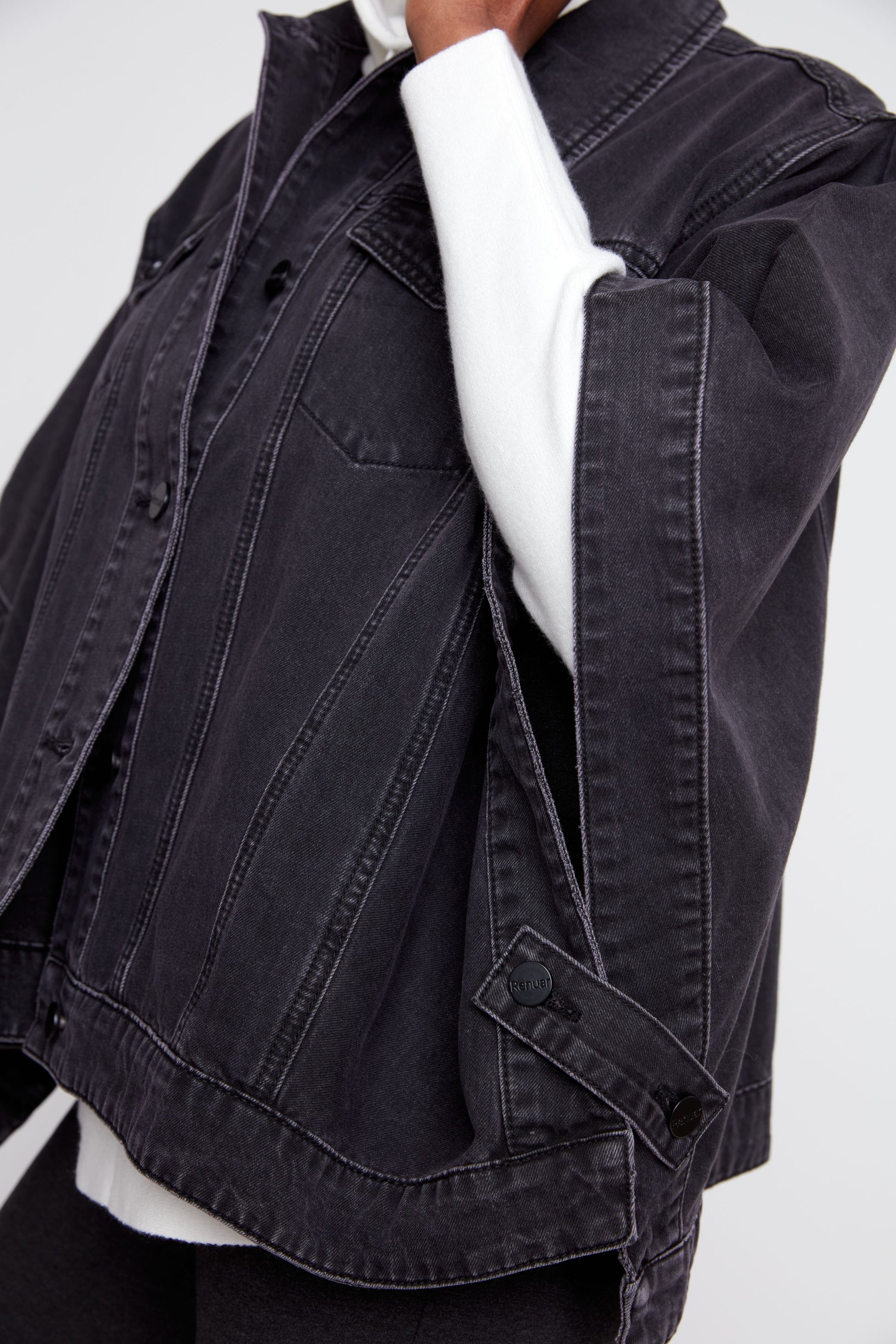 A close-up of a person wearing a dark washed denim jacket over a white long-sleeve top, showing the texture and details of the jacket.