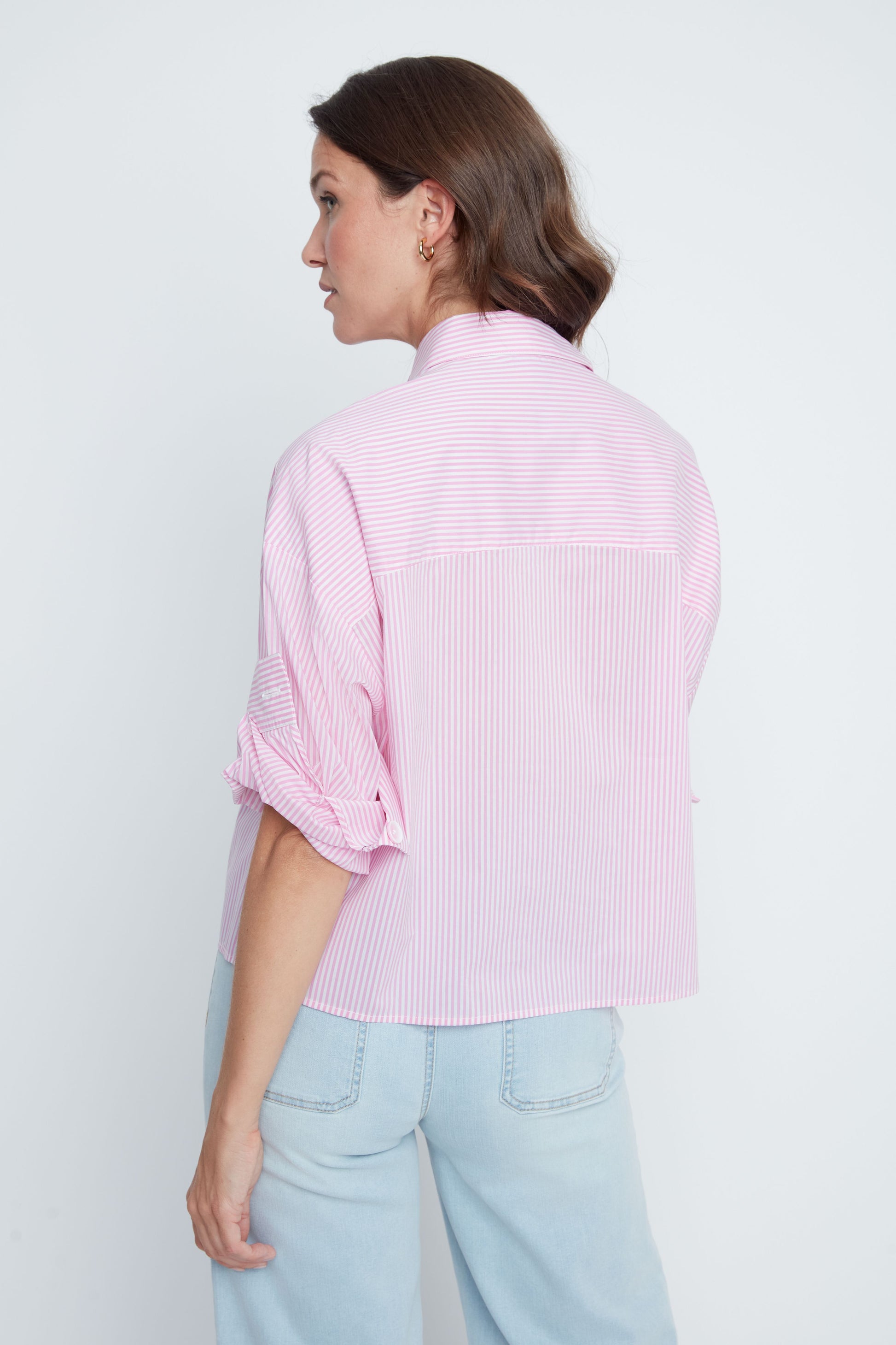 Woman wearing a light pink striped shirt and light blue jeans against a white background