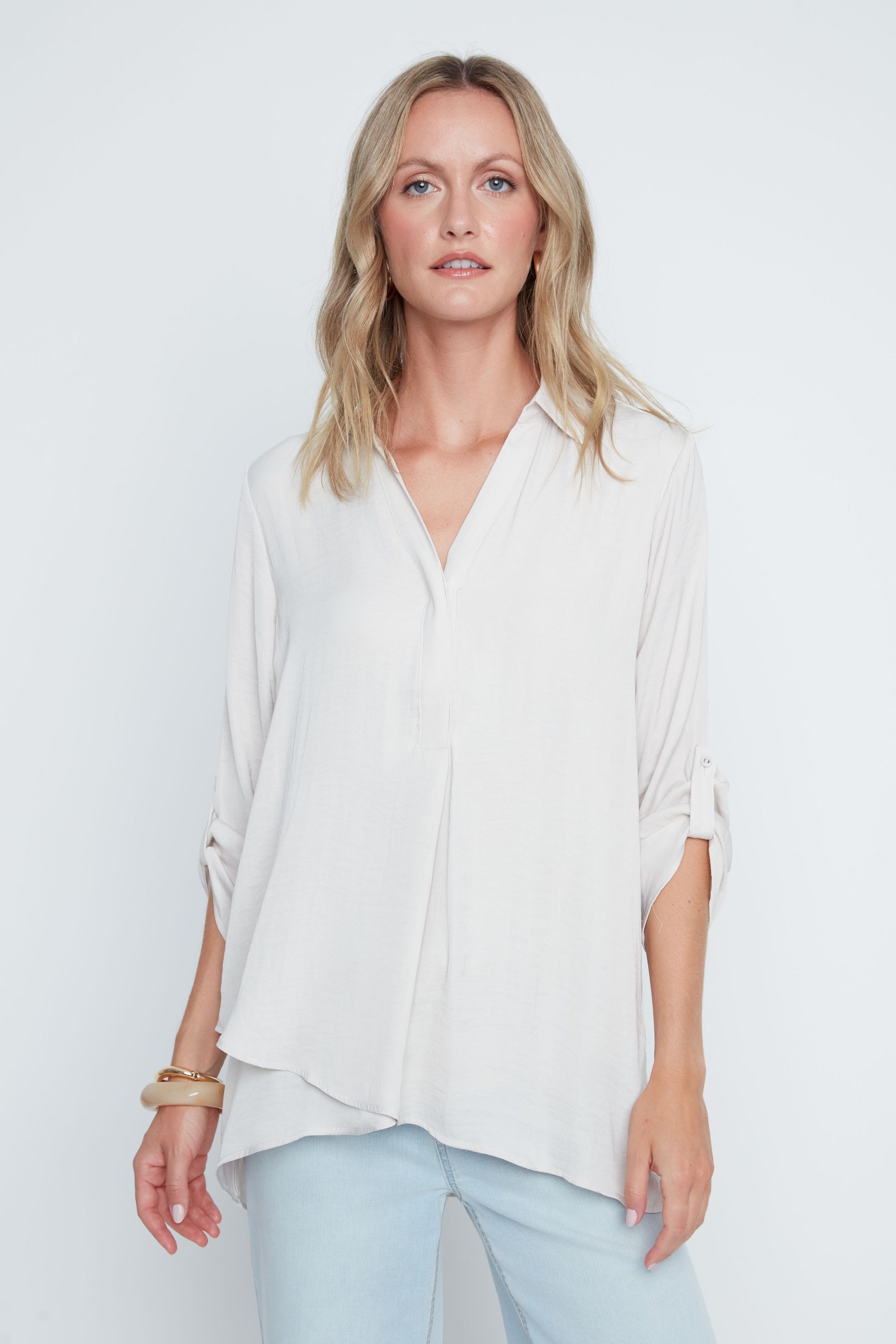 Woman wearing a white blouse and light blue jeans against a plain background