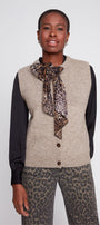 Woman wearing a beige vest over a black long-sleeve shirt with a leopard print scarf and pants on a white background