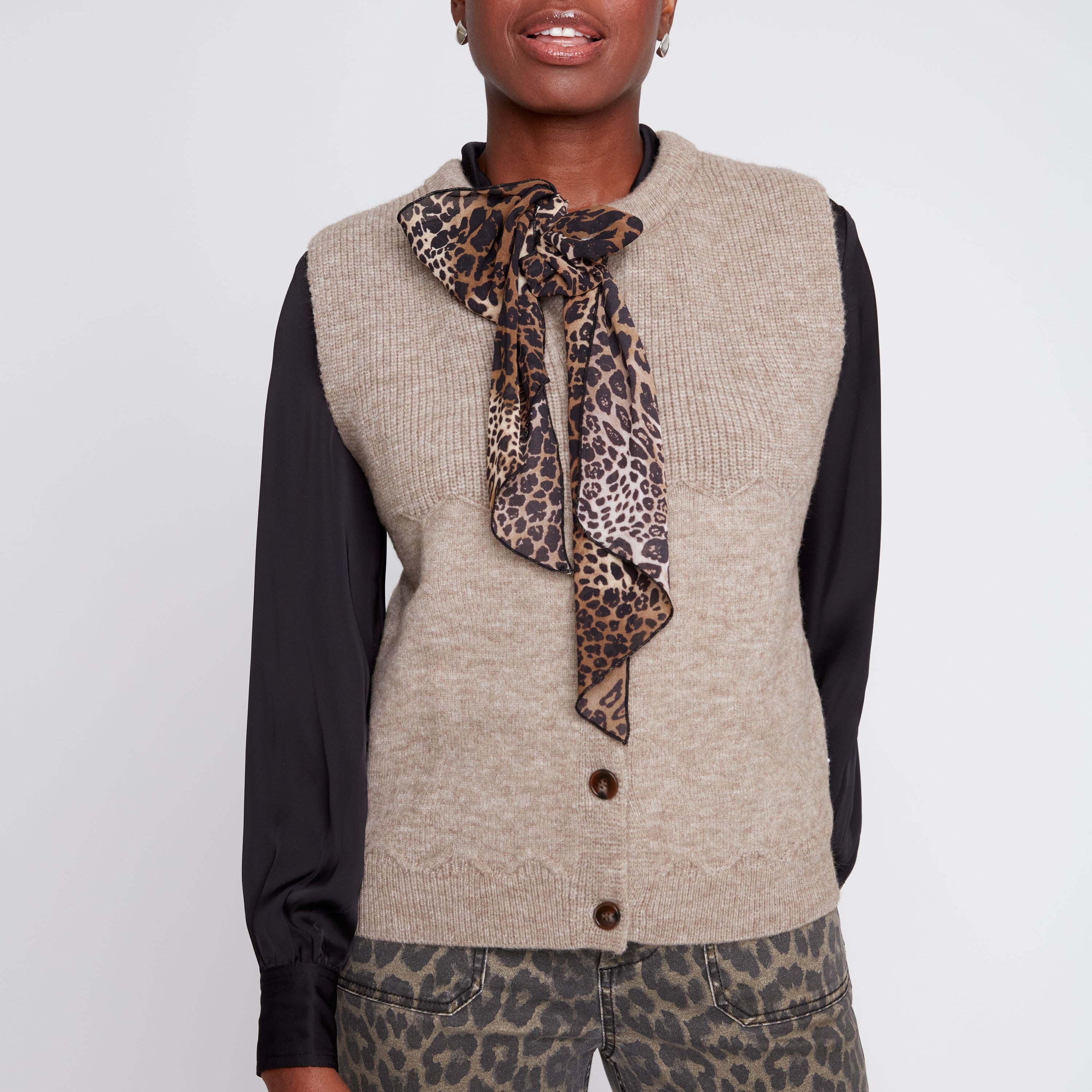 Woman wearing a beige vest over a black long-sleeve shirt with a leopard print scarf and pants on a white background