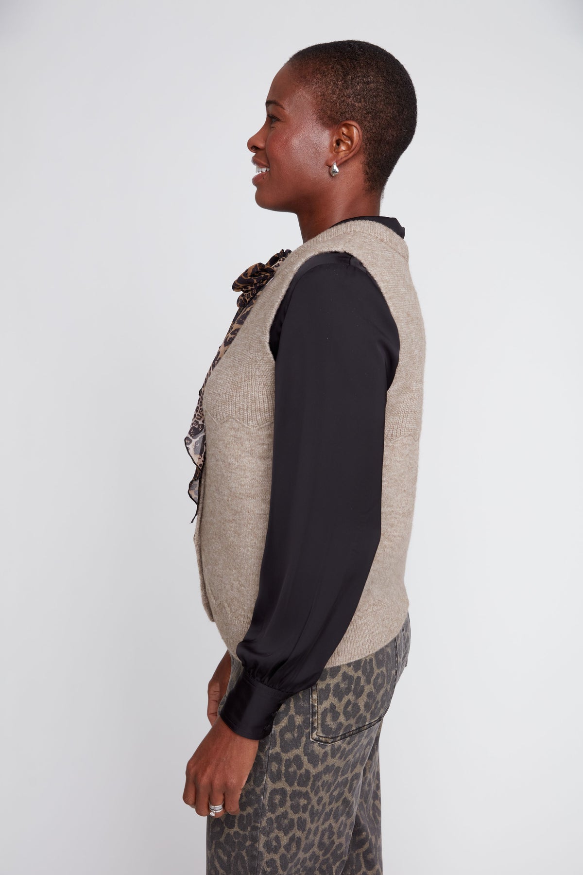 Person wearing a beige vest over a black shirt with a leopard print skirt on a white background