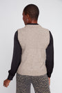 Person wearing a beige knitted vest over a black long-sleeve shirt on a white background