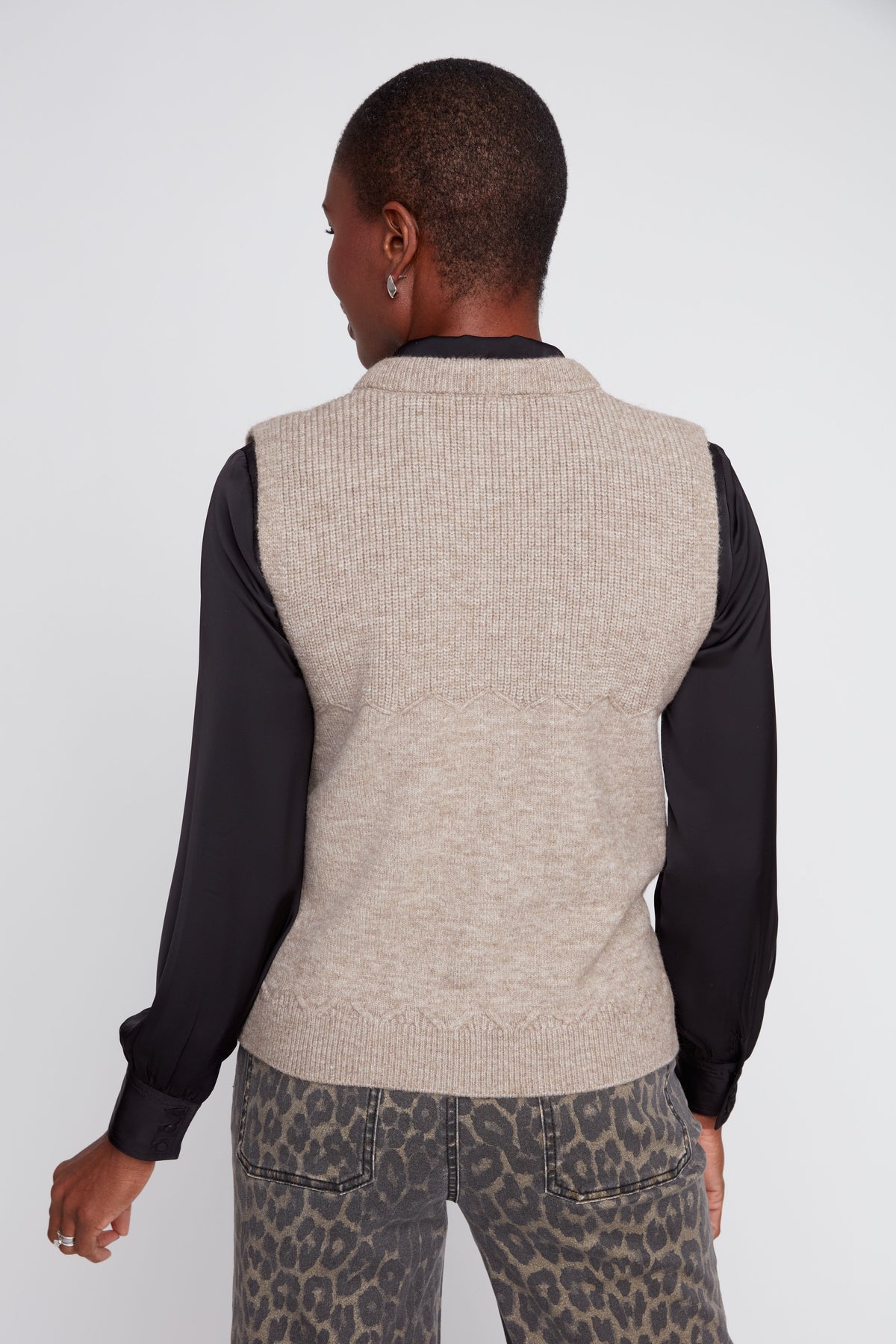 Person wearing a beige knitted vest over a black long-sleeve shirt on a white background