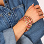A close-up of a person's arm wearing a stack of gold bangles decorated with red and white checkered patterns, styled with a blue denim shirt.