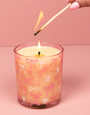 Candle with pink bow pattern being lit with a match against a pink background