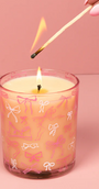 Candle with pink bow pattern being lit with a match against a pink background