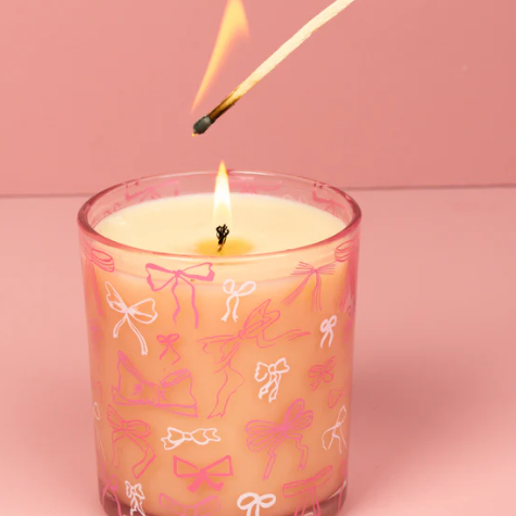 Candle with pink bow pattern being lit with a match against a pink background