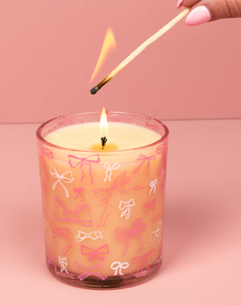 Candle with pink bow pattern being lit with a match against a pink background