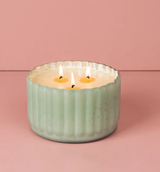 Green candle in a textured container on a pink background
