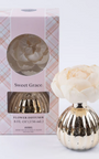 Gold flower diffuser with a white flower on top next to its packaging on a white background